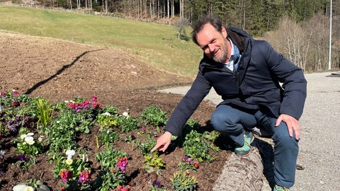 Thomas Kreuder in der Hocke neben einem Beet mit frisch gepflanzten Frühlingsblühern. Sie sind die ersten Vorboten der Gartenschau Freudenstadt Baiersbronn.