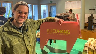 Martin Lai von Südhang Kaffee in Tübingen. Mit einer Holzkuh möchte er auf ungerechte, unterschiedliche besteuerung von Kuhmilch und Hafermilch aufmerksam machen.