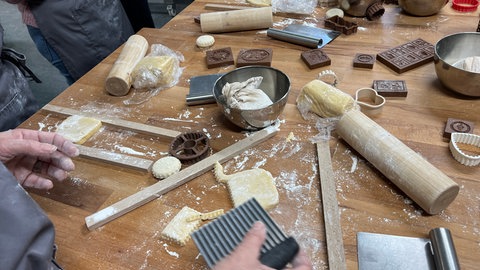 Auf dem Tisch beim Backkurs in Münsingen liegen Teig, ein Teigschaber, Holzstäbe, eine Teigrolle und Model für die Springerle. 