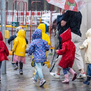 Eine Kindergartengruppe rennt während eines einsetzenden Gewitterregens über den Bürgersteig. (Symbolbild)