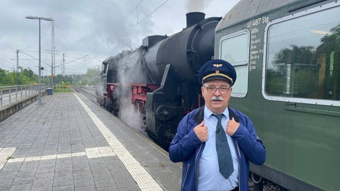Am Bahnsteig in Horb (Kreis Freudenstadt) steht Bernd Günther vor der Lokomotive. Er trägt Krawatte und eine Eisenbahnermütze.