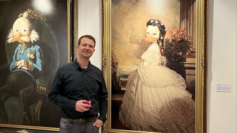Ein Mann steht vor zwei großen Gemälden mit Kaiserin Elisabeth und Kaiser Franz Joseph, die zu Enten umgestaltet wurden.