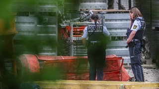 Zwei Polizistinnen stehen auf der Hochbrücken-Baustelle in Horb (Kreis Freudenstadt) neben einer Gondel. Drei Männer sind in einer Gondel abgestürzt und tödlich verunglückt.