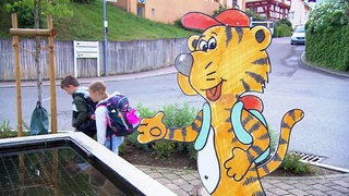 Zwei Kinder laufen an einem Tiger-Schild vorbei. Die Grundschule Bodelshausen hat sich was gegen Elterntaxis überlegt.