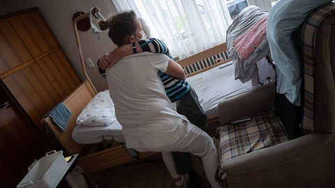 Eine Pflegerin hilft einer Person aus dem Bett. 