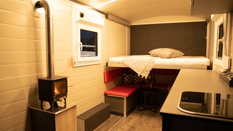 Ein Innenraum eines Wohnanhängers mit Ofen, Bett und Küchenzeile. "TheCuber" aus Engstingen (Kreis Reutlingen) produzieren fahrbare Tiny Houses.