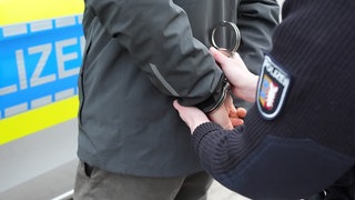 Eine Polizistin legt einem Mann Handschellen an. 
