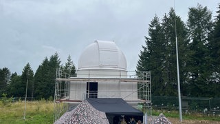 Zu sehen ist ein Betonturm mit einer weißen Kuppel als Dach. In den Türmen auf dem Truppenübungsplatz Meßstetten werden Weltraumteleskope eingebaut.