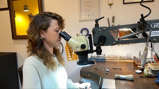 Maren Baum sitzt an ihrer Werkbank und schaut durch ein Mikroskop. Sie ist Edelsteinfasserin in Tübingen. 