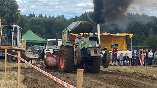 Ein grüner Traktor zieht das tonnenschwere Gewicht, muss volle Leistung geben, die Vorderräder gehen in die Höhe  