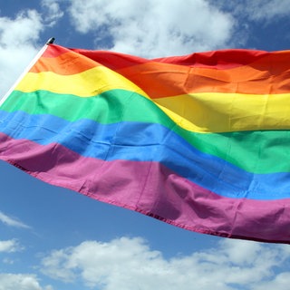 Eine Regenbogenflagge weht vor blauem Himmel.