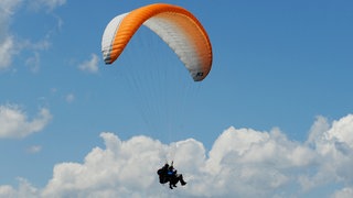 Symbolbild: Vor blauem Himmel hängen zwei Menschen an einem Gleitschirm. Bei einem Tandemflug bei Hausen im Killertal sind zwei Personen schwer verletzt worden.