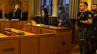 Ein Mann mit Handschellen im Gerichtsraum. Rechts daneben sind zwei Justizvollzugsbeamte. Links neben dem Angeklagten steht die Verteidigerin. Der Angeklagte wurde wegen Körperverletzung und Vergewaltigung zu elf Jahren Haft verurteilt.