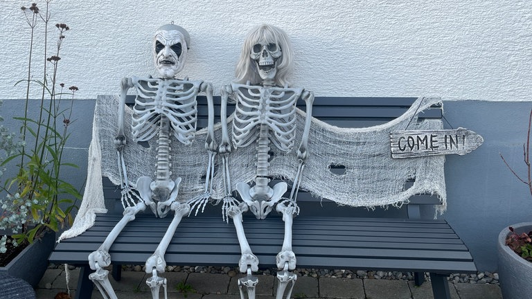 Zwei Skelette sitzen an Halloween auf einer Bank vor einem Haus in Reutlingen-Degerschlacht. 