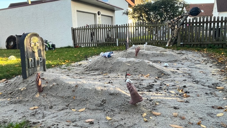 Gräber aus Sand, aus denen Hände und Füße ragen: Mehrere Häuser in Reutlingen-Degerschlacht sind an Halloween gruselig geschmückt.