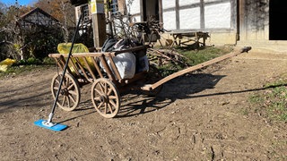 Ein alter Holzwagen mit großen Rädern steht im Freilichtmuseum Neuhausen ob Eck. Darauf: Putzsachen und Tüten.