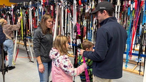 Eine Familie steht, mit Skistöcken in der Hand, vor einer riesigen Auswahl weiterer Skistöcke. Sie sind bei der Skibörse in Albstadt-Tailfingen.