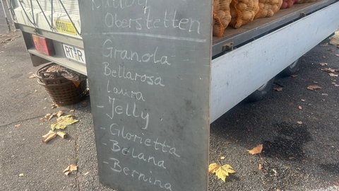 Auf einem Schild sind Rudolfs Kartoffelsorten aufgelistet. Er verkauft acht verschiedene Sorten an seinem Stand.
