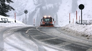 Ein Fahrzeug des Winterdienstes im Einsatz auf einer Straße mit Schnee. 