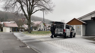 Auf einem Firmengelände auf der Schwäbischen Alb in St. Johann steht ein Polizist vor einem Polizeiauto. Hier wurden die toten Söhne des Tatverdächtigen gefunden.
