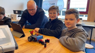 David Honold unttersucht an einem Tablet, wo die richtigen Einstellungen für den Roboter sind, den die beiden Schüler neben ihm gerade zusammenbauen. 