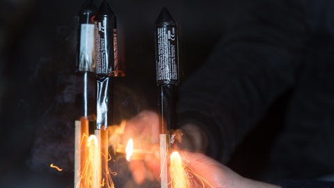 Eine Hand zündet Silvesterraketen an - was nicht ungefährlich ist.