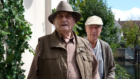 Walter Schultheiß gemeinsam in einer Filmszene mit Dietz-Werner Steck in der Serie "Laible und Frisch". Im Hintergrund ein Baum mit grünen Blättern.  