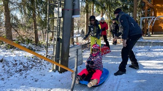 Ein Lift zieht ein Kind auf dem Schlitten den verschneiten Berg hinauf. Auch in Holzelfingen auf der Alb ist der WInter angekommen. Hunderte Rodeln im Schnee.