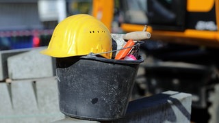 Ein gelber Bauarbeiterhelm liegt auf einem Eimer eines Maurers auf einer Baustelle