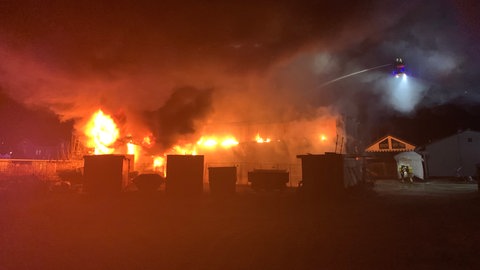 Flammen und Rauch dringen aus einer Lagerhalle. Die Feuerwehr im Einsatz bei einem Großbrand in Lichtenstein im Kreis Reutlingen.