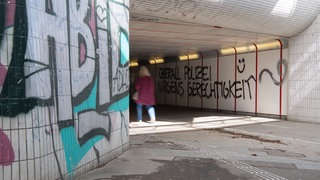 Graffiti an den Wänden einer Unterführung in Tübingen, im Hintergrund geht eine Person durch den Tunnel.