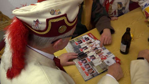 Der Zunftmeister von Rottenburg im Häs schaut ein Sticker-Album an. Die Zunft hat ein eigenes Sammelalbum mit allen Fasnetsfiguren. Seither ist Rottenburg im Sammelfieber.