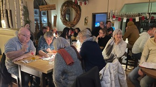 In einer Kneipe in Horb sitzen Menschen an Tischen. Sie nehmen am Pub-Quiz teil. Die Fragen drehen sich um die Landtagswahl von Baden-Württemberg.