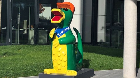 Ein grün-gelbes Maskottchen vor einem Gebäude. Ein Trossino ist in Trossingen von Unbekannten angezündet worden.