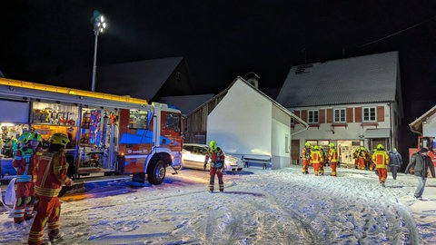 Feuerwehrleute in leuchtenden Uniformen laufen vor dem Feuerwehrhaus in Rosenfeld-Brittheim über schneebedeckten Boden.