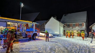 Feuerwehrleute in leuchtenden Uniformen laufen vor dem Feuerwehrhaus in Rosenfeld-Brittheim über schneebedeckten Boden.