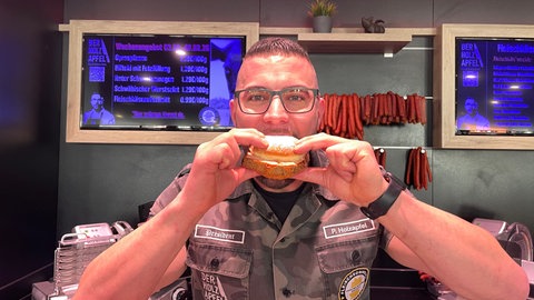 Metzgermeister Patrick Holzapfel aus Mössingen beißt in einen Berliner, der mit Fleischkäse belegt ist. Er bietet die Kreation zur Fasnet an.