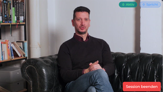 Ein digitaler KI-Avatar von Maxim Probojcevic sitzt auf einem Sofa und spricht in die Kamera. Über eine Weboberfläche ist eine Interaktion möglich.