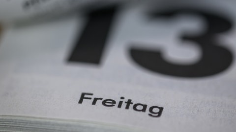 Kalenderblatt mit der Zahl 13, darunter das Wort „Freitag“, unscharf im Hintergrund.