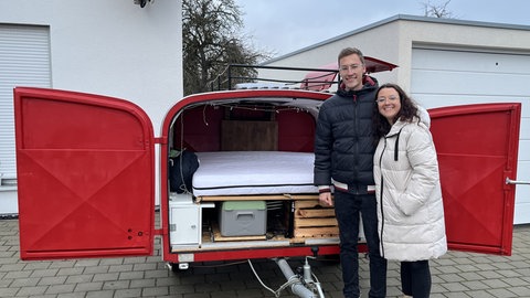 Ein Mann und eine Frau stehen vor ihrem Campingwagen. Hannes hat Sophia einen Antrag gemacht und dafür einen Verlobungsring in die Stratosphäre geschickt.
