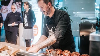 Ein Koch beim Burger-Battle belegt Brötchen mit Fleisch. Der Sigmaringer hat bei der Messe INTERGASTRA in Stuttgart den ersten Platz mit seinen Burgern gemacht.