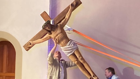 Das große Kreuz wird von zwei Männern beim letzten Gottesdienst vom Altar genommen.