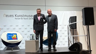 Wolfgang Grupp und Gregor Gysi nach dem Gespräch, Arm in Arm auf der Bühne.