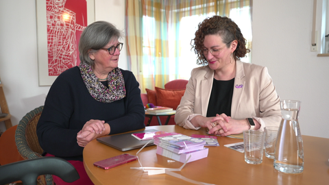 Zwei Frauen der Regionalgruppe Tübingen sitzen am Tisch, vor ihnen liegen Flyer über die sie sprechen
