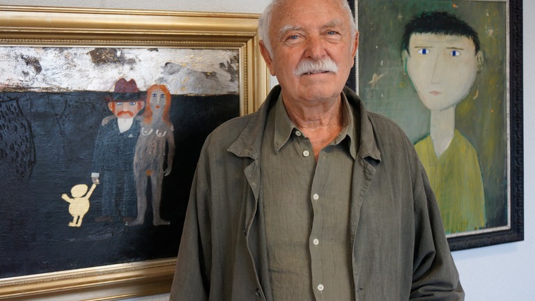 Der Künstler Janosch steht vor zwei seiner Bilder. Das Neue Kunstmuseum Tübingen macht zu seinem 95. Geburtstag eine Sonderschau seiner Werke. 150 Kinder feiern mit Tigerente, Bär und Herrn Wondrak.