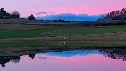 Ein kleiner See, umgeben von Wiese bei Sonnenuntergang. Der Märzenbronnen bei Burladingen-Salmendingen kommt nur nach Regen oder Schneeschmelze zum Vorschein. 