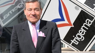 Ex-Trigema Chef Wolfgang Grupp vor dem Firmenlogo