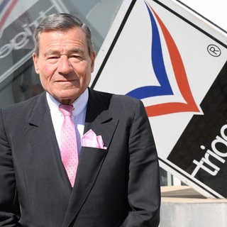 Ex-Trigema Chef Wolfgang Grupp vor dem Firmenlogo