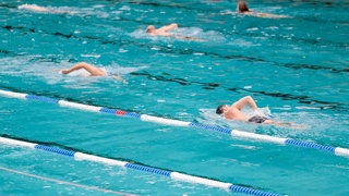 Menschen schwimmen in einem Schwimmbecken. In Tübingen soll das Hallenbad Nord saniert werden. Der geplante Neubau des Hallenbades Süd liegt weiter auf Eis. (Symbolbild)