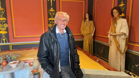 Gerd Schollian sitzt auf einer kleinen Mauer in einem Raum des Römischen Museums in Hechingen-Stein. 